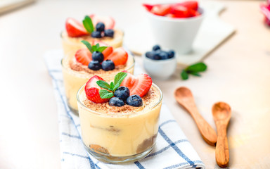 homemade, exquisite dessert tiramisu in glasses decorated with strawberry, blueberry, mint on white wooden table