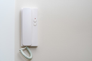 Intercom hung on a white wall at the door of home.