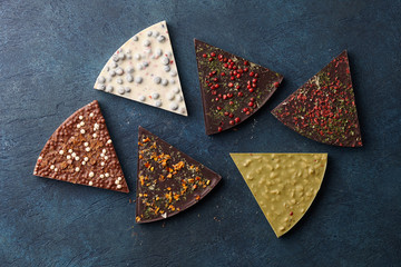 Chocolate triangle shaped pieces with diverse kinds of toppings on blue background, top view