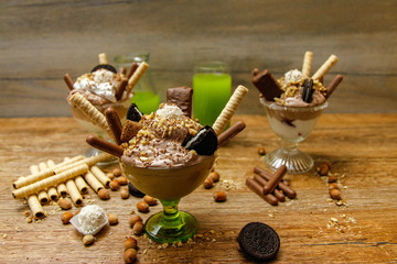 Cup of ice cream with cookies. Wooden background and different cookies and hazelnuts on table.