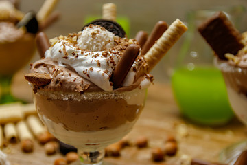 Cup of ice cream with cookies. Wooden background and different cookies and hazelnuts on table.