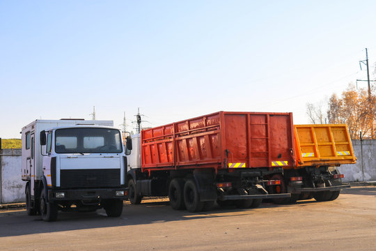 Large heavy cargo trucks with cabs and trailers, dump trucks stand in a row in the parking lot ready for delivery
