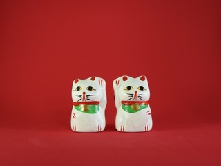 Two little Maneki Neko, Japanese lucky cats, amulets that bring good luck, protection, prosperity, health and happiness. Red background.