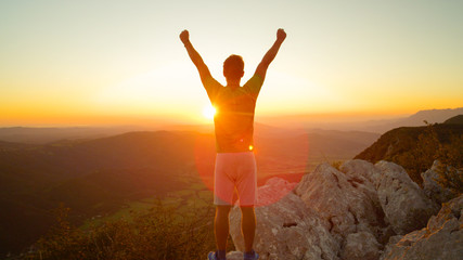 LENS FLARE: Happy hiker raises his arms overhead after seeing the sunset.