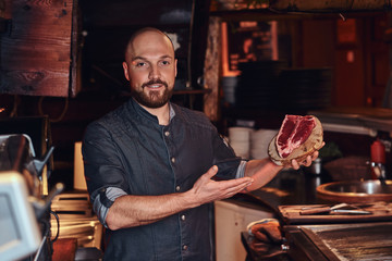 Chef presenting a fresh steak before cooking and looking at a camera in a restaurant kitchen.