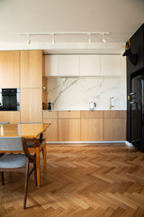 Stylish and cozy scandinavian dining room and kitchen with design family table, chairs and lamp. White walls and brown wooden parquet.
