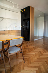 Stylish and cozy scandinavian dining room and kitchen with design family table, chairs and lamp. White walls and brown wooden parquet.