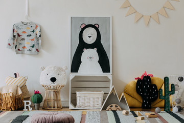 Stylish scandinavian kid room with mock up photo poster frame on the pattern wall, boxes, teddy bear and toys. Cute modern interior of playroom with white walls, wooden accessories and colorful toys.
