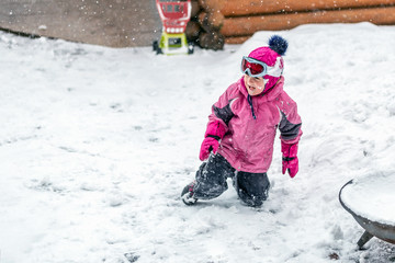 Fototapeta na wymiar Cute little girl in pink sport suit having fun playing outdoors during snowfall in winter. Children winter seasonal outdoor activities