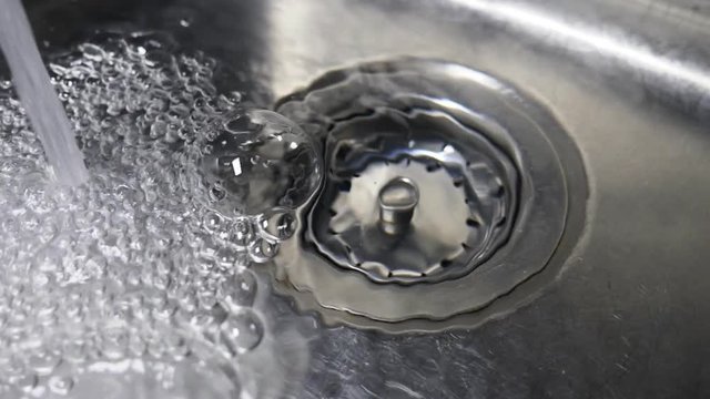 Slow motion kitchen sink. Water filling up sink with bubbles and drain.