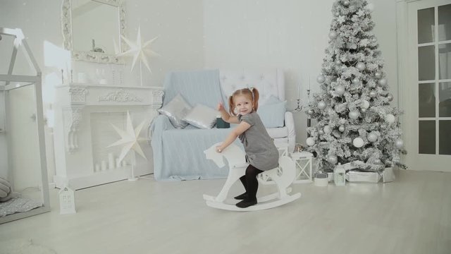 Very beautiful little girl riding on a wooden horse in the New Year's room and smiling.