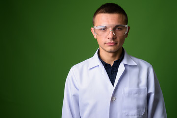 Young handsome man doctor wearing protective glasses against gre