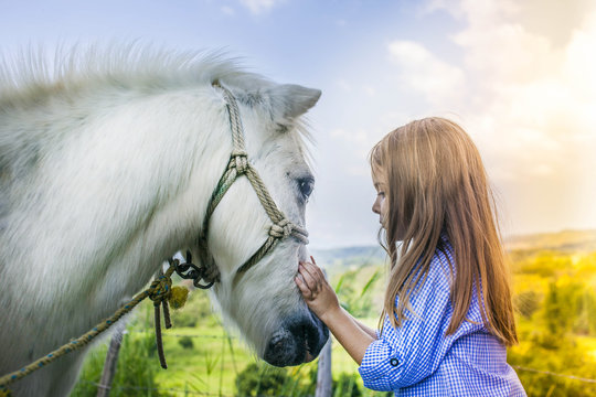 h&uuml;bsches, blondes Kind streichelt ein Pferd