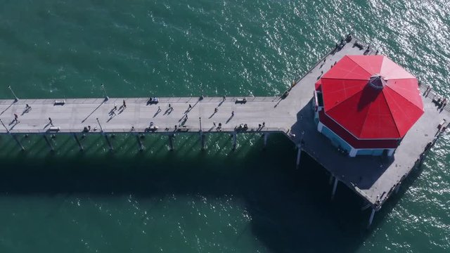 Drone aerial of tourists walking near restaurant on end of long ocean pier 