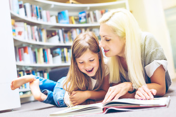 Mother with daughter read book together in library