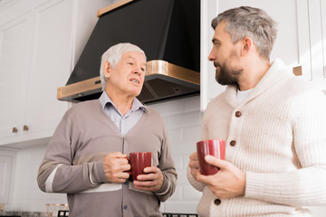 Warm toned waist up portrait of senior man talking to son in cozy kitchen 
Keywords: