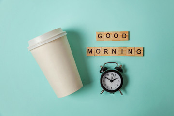 Simply flat lay design paper coffee cup and alarm clock on blue pastel colorful trendy background. Takeaway drink and breakfast beverage. Good morning wake up awake concept. Top view copy space