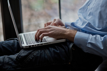 A man sits on a windowsill and works on a laptop. Beautiful man's wrist. Long fingers of a young man.