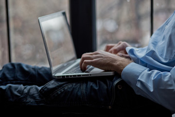 A man sits on a windowsill and works on a laptop. Beautiful man's wrist. Long fingers of a young man.