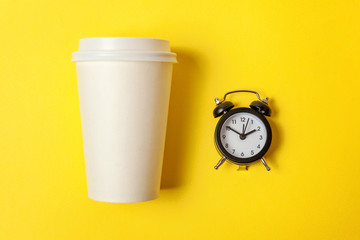 Simply flat lay design paper coffee cup and alarm clock on yellow colorful trendy background....