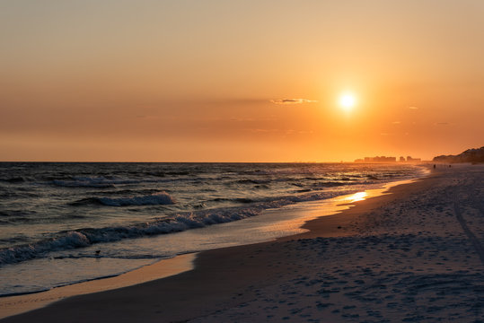 Orange yellow sunset in Santa Rosa Beach, Florida with Pensacola coastline coast cityscape skyline in panhandle with ocean gulf mexico waves, silhouette of buildings