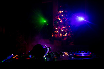 Dj mixer with headphones on dark nightclub background with Christmas tree New Year Eve. Close up view of New Year elements on a Dj table. Holiday party concept.