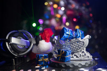 Dj mixer with headphones on dark nightclub background with Christmas tree New Year Eve. Close up view of New Year elements on a Dj table. Holiday party concept.