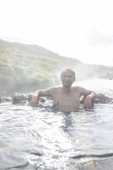 Young happy man swimming bathing in Hveragerdi Hot Springs on trail in Reykjadalur, during autumn summer morning day in south Iceland, golden circle, rocks, vertical view