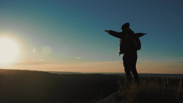 Silhouette of person in mountain. Young man with backpack standing with raised hands on top of a mountain. Sport and active life.