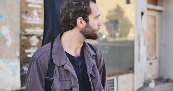 Bearded man with guitar strapped to his back turns to look at woman and window reflection of woman walking away towards the bus