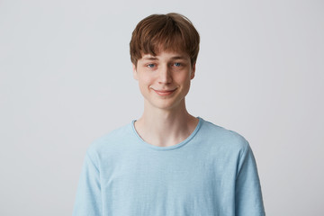 Portrait of attractive smiling blue-eyed young guy with short haircut wears blue t-shirt standing...