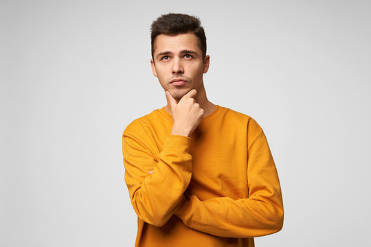 Handsome Attractive Young Man Ponders Over A Gift For A Girl For A New Year Or Birthday, Remembers The Latest Events, Thinking Of Something Important Holding His Chin, Looks Into The Distance