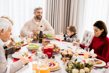Warm-toned portrait of big happy family enjoying Christmas dinner together, focus on smiling man in head of table