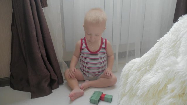 Little baby boy playing with colourful small blocks of a constructor in the room on the floor. Kid playing with colored blocks of a constructor on floor in children room.