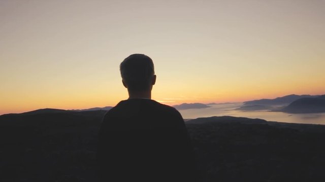 Man overlooking the sunset as the camera moves behind him