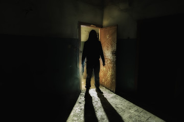 Creepy silhouette of unknown man with knife in dark abandoned building. Horror about maniac concept...