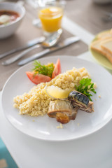 bulgur with vegetables and rolls of baked fish with corn, tomatoes and lemon on a white plate with orange juice
