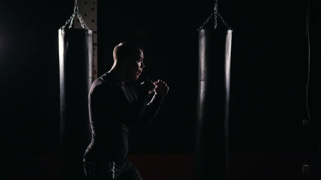 Boxer doing shadow Boxing in a dark room. Man of athletic build makes a punch. Dramatic lighting night training male