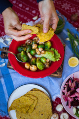Woman hands break, split Mexican tacos - corn flat breads. Vegan happy Christmas food lunch on red tablecloth. Vegetarian traditional holiday dinner. Baked, roasted, grilled vegetables mix assortment.