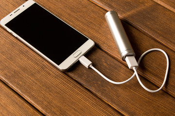 Silver power bank charging smartphone on wooden table