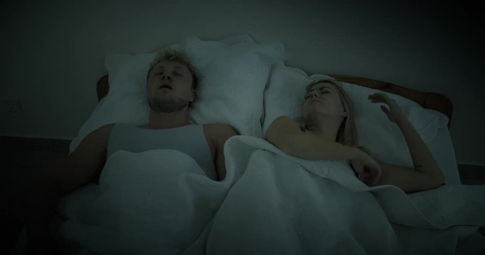 A woman is woken up by her partner's snoring, she is annoyed, rolls over and covers her ears with her hands