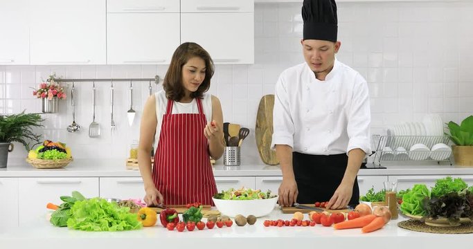 Asian chef demonstrate how to cut tomatoes pieces for beautiful woman in cooking class in white clean modern kitchen.