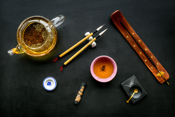 Chinese or japanese traditions. Calligraphy and tea ceremony concept. Special writting pen, ink near teapot and cup of tea, insense on black background top view