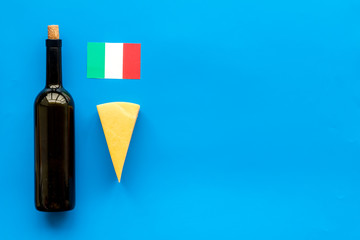 Gastronomical tourism. Italian food symbols. Italian flag, cheese parmesan and bottle of red wine on blue background top view space for text