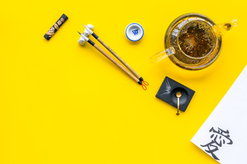 Lesson of calligraphy concept. Paper with hieroglyph love near writing accessories, teapot and cup...