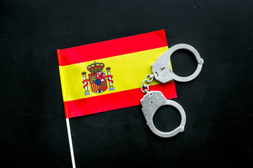 Violation of law, law-breaking concept. Metal handcuffs on Spanish flag on black background top view