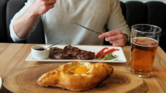 Man eating roasted meat, tandoori bread, drinking bear in Georgian restaurant.