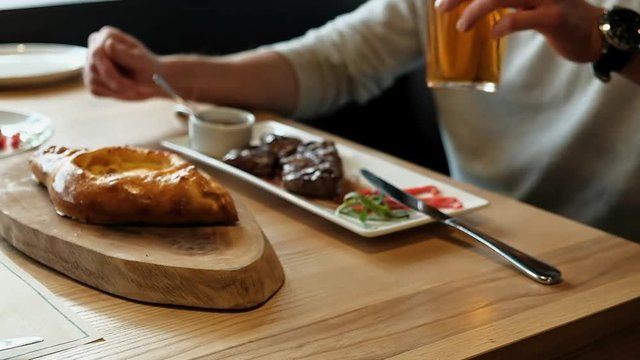Man eating roasted meat, tandoori bread, drinking bear in Georgian restaurant.