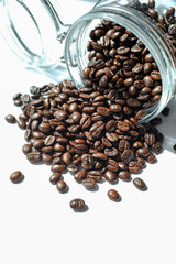 Dark roasted coffee bean spill of a glass jar on white background