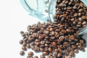 Dark roasted coffee bean spill of a glass jar on white background